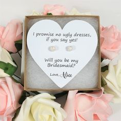 a heart shaped box with two earrings in it next to pink roses and white flowers