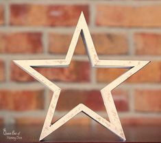 a white wooden star sitting on top of a table next to a brick wall in front of a window