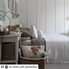 a teddy bear sitting in a basket next to a bed with white sheets and pillows