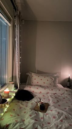 a cat laying on top of a bed next to a window with candles in it