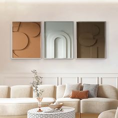 three abstract paintings hang on the wall above a couch and coffee table in a living room