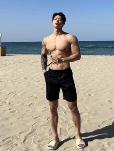 a man standing on top of a sandy beach next to the ocean wearing flip flops