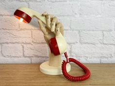 a red and white hand holding an old fashioned telephone on a wooden table next to a brick wall