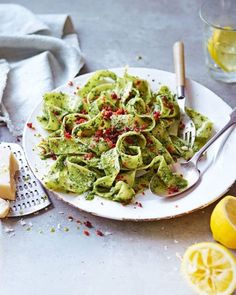 a white plate topped with pesto pasta next to sliced lemons and parmesan cheese