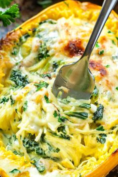 a spoon in a yellow casserole dish with spinach and cheese on top