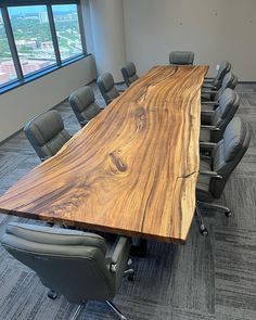 an empty conference room with chairs and a large wooden table in front of a window