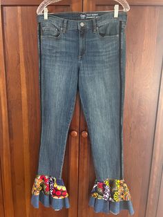 a pair of jeans with ruffled hems hanging on a wooden closet door in front of a wood paneled wall