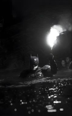 black and white photo of batman in the water with light shining from his chest up