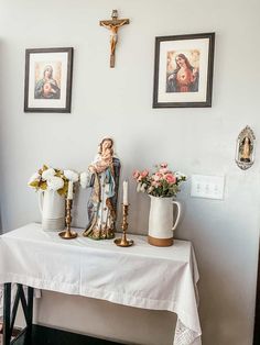 a table with flowers and statues on it in front of two framed pictures above the table