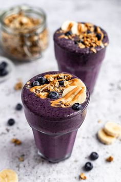 two glasses filled with blueberry smoothie topped with banana slices and granola pieces