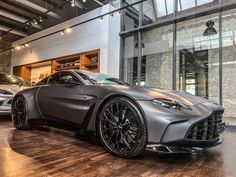 two silver sports cars in a showroom with wooden floors and large windows on the wall