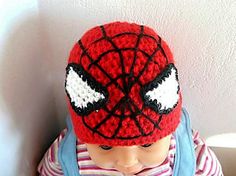 a small child wearing a spiderman hat with eyes on it's face, sitting in front of a white wall