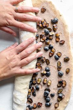 two hands reaching for nuts on top of a flat bread dough with blueberries and pistachios