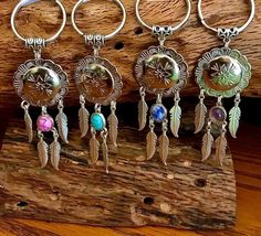 six different colored beads and charms hanging on a piece of wood with a wooden plank in the background