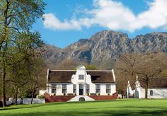 a large white house sitting in the middle of a lush green field with mountains behind it