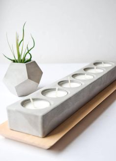 a concrete candle holder with three votive candles and a plant in the middle on a white surface