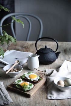 a table topped with plates and bowls filled with food next to a tea pot on top of a wooden table