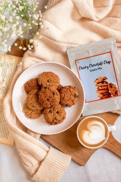 chocolate chip cookies on a white plate next to a cup of coffee and a book