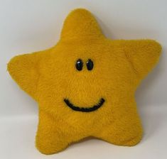 a yellow stuffed star with black eyes and a smile on it's face, sitting against a white background