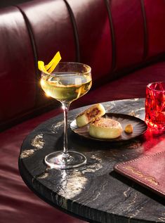 a table topped with a plate of food next to a glass of wine and a drink