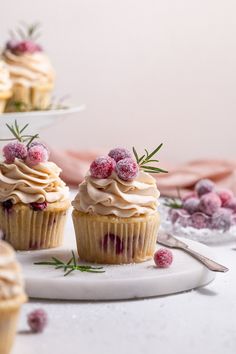 three cupcakes with frosting and raspberries are on a white plate