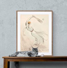 a cat laying on top of a wooden table next to a drawing and a tennis racket