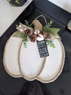 a white pumpkin decorated with pine cones and twine on top of a black counter