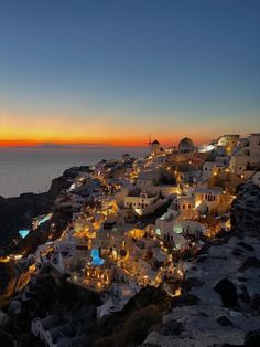 the sun is setting over some white buildings on top of a hill near the ocean