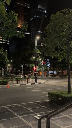 an empty city street at night with traffic lights and benches in the foreground, surrounded by tall buildings