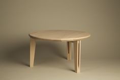 a round wooden table sitting on top of a white floor next to a gray wall