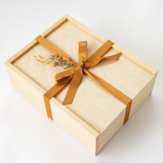 a wooden box with an orange ribbon tied around the lid and inside, sitting on a white surface