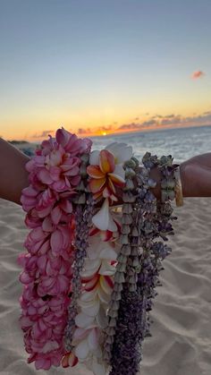 a person holding flowers on the beach at sunset