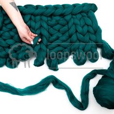 a person is knitting green yarn on top of a white surface with two hands holding the yarn