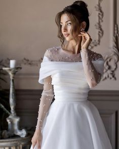 a woman in a white dress is talking on her cell phone while standing next to a table