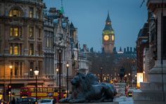 there is a statue of a lion in the middle of this street with a clock tower in the background