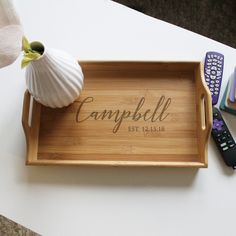 a personalized bamboo tray with the word campbell on it and some remotes next to it