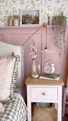 a bedroom with pink walls and flowers on the nightstand next to it is decorated in white