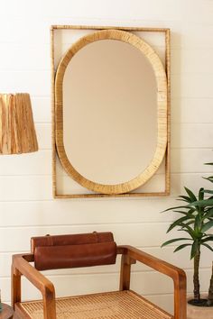 an oval mirror hanging on the wall above a wooden chair with a leather seat in front of it