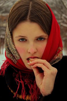 a young woman wearing a red scarf and eating something with her hand in her mouth