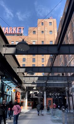 people are walking on the sidewalk under an overpass in front of a building with a market sign above it