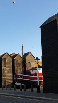 a red and white boat sitting on the side of a road next to wooden buildings