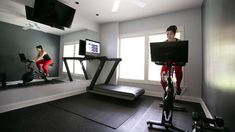 a woman is running on a treadmill in a room with mirrors and televisions