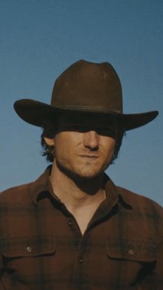 a man wearing a cowboy hat and looking at the camera with a blue sky in the background