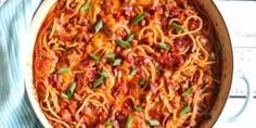 a pan filled with spaghetti and sauce on top of a blue striped towel next to a wooden table