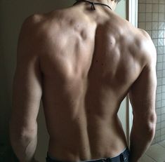 a man with no shirt standing in front of a bathroom mirror looking at his back