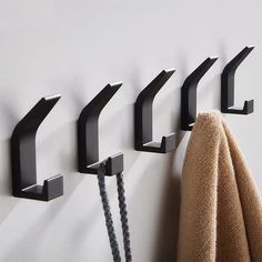 four black hooks are hanging on the wall next to a towel and two brown towels