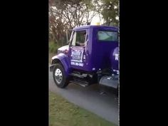 a purple truck driving down a road next to some grass and trees in the background