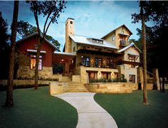 a large house sitting in the middle of a lush green field next to tall trees