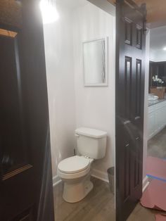 a white toilet sitting inside of a bathroom next to a wooden door in a room