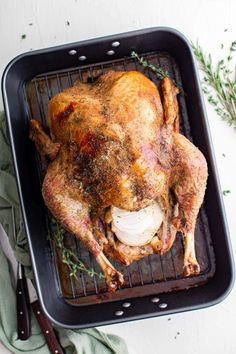 a roasting pan with a whole chicken on it and garnished with herbs